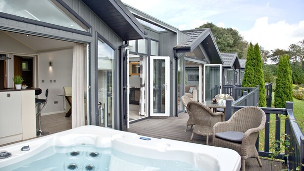 A modern outdoor deck with a hot tub, wicker furniture, and a glass-enclosed patio area. - Watermouth Lodge, Kentisbury Grange (Barnstaple)