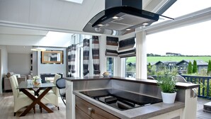 A modern kitchen with a large island, a built-in stove, and a view of the countryside. - Watermouth Lodge, Kentisbury Grange (Barnstaple)