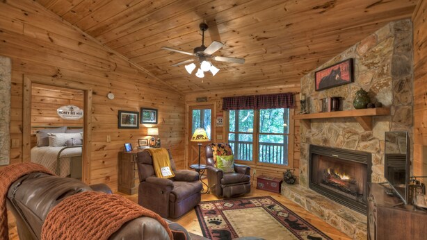 A cozy cabin interior with a fireplace, leather furniture, a stone wall, and a ceiling fan.