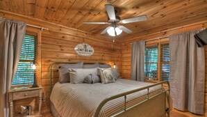A wooden cabin bedroom with a bed, a ceiling fan, and a sign on the wall.