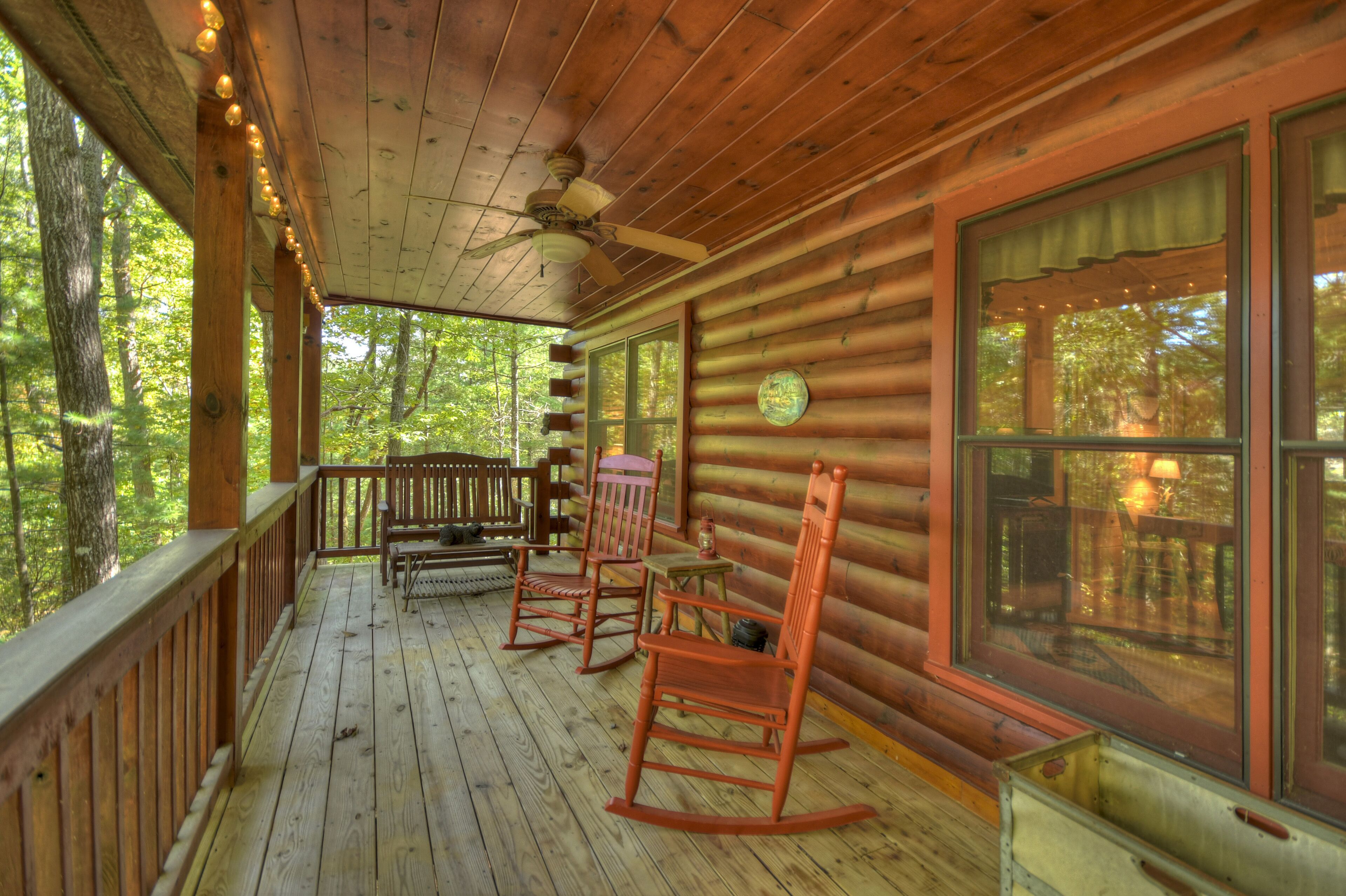 A wooden cabin with a porch, rocking chairs, and a ceiling fan.