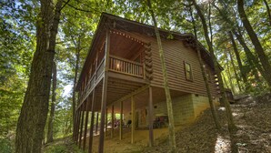 A wooden cabin with a balcony, surrounded by trees in a forest.