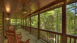 A wooden cabin with a porch, wooden chairs, and a view of a forest.
