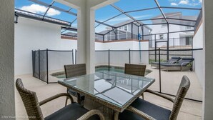 A glass-top table with wicker chairs, a pool, and a view of neighboring houses.