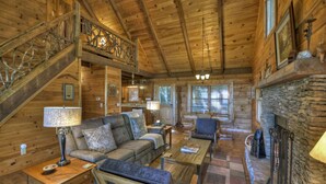 Interior acogedor de una cabaña de troncos con una escalera de madera, una chimenea de piedra, un sofá y una mesa de centro.