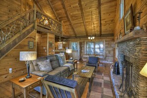 A cozy log cabin interior with a wooden staircase, a stone fireplace, a sofa, and a coffee table.