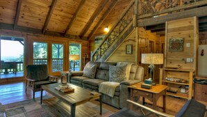 Interior acogedor de una cabaña con techo de madera, un sofá, una mesita de café y una escalera que sube a una zona tipo loft.