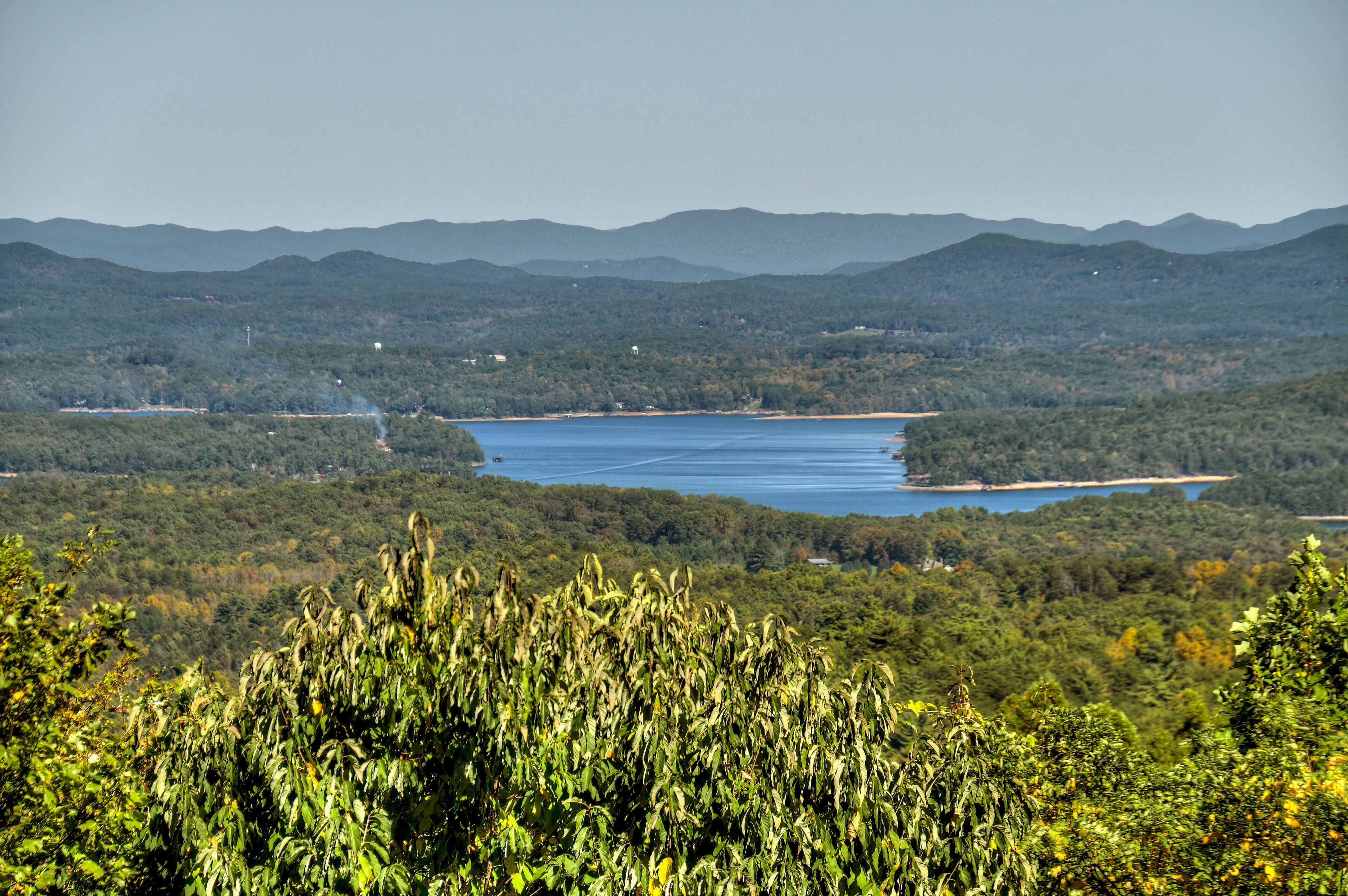 A panoramic view of a lake surrounded by dense forest and distant mountains.