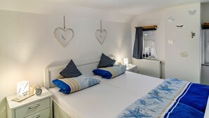 Une chambre à coucher comprenant un lit, deux tables de chevet, une commode, une fenêtre avec des rideaux et des éléments de décoration murale, notamment des cœurs et des papillons.
