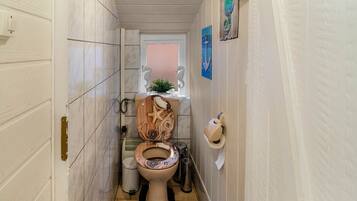 Ein schmales Badezimmer mit Toilette aus Holz, einem kleinen Fenster und maritimen Dekorationen.
