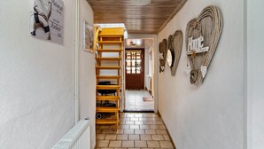 Un couloir étroit avec un escalier en bois, une porte au fond et des panneaux décoratifs en forme de cœur accrochés aux murs.