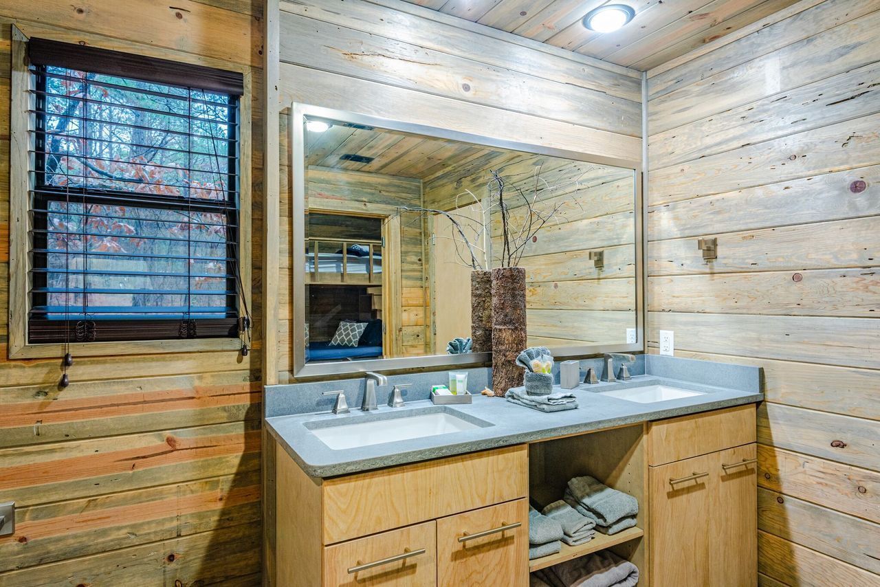 Une salle de bain rustique, avec des murs en bois, un grand miroir, deux lavabos et des meubles de rangement en bois.