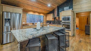 A modern kitchen with a granite countertop, stainless steel appliances, and a large window overlooking a forest.