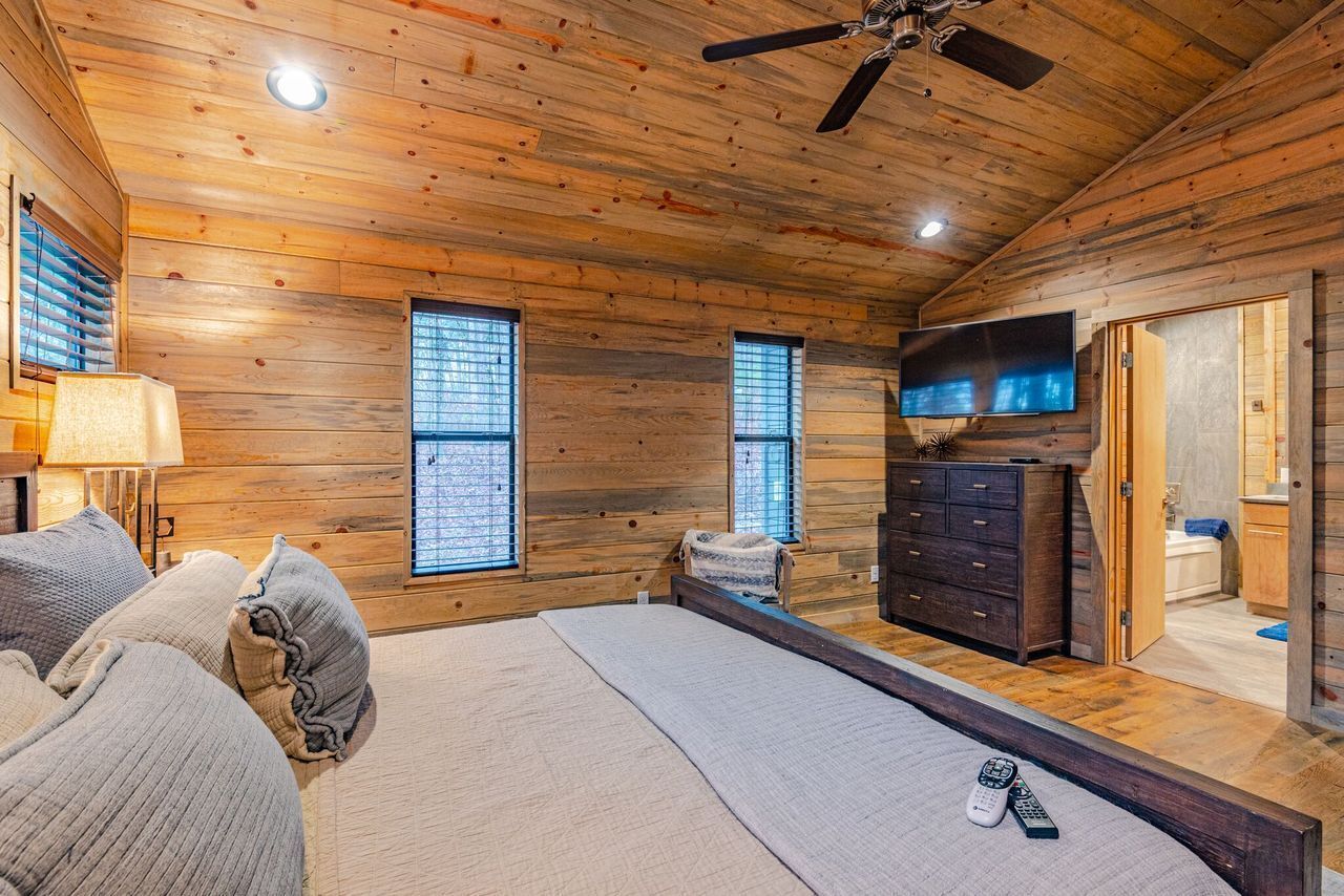 A log cabin bedroom with a bed, dresser, TV, and a ceiling fan.