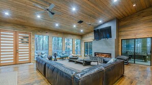 A spacious living room with a large leather sofa, a fireplace, and a television mounted on the wall.