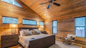 A bedroom with a wooden ceiling, a bed, two bedside tables, and a window with blinds.