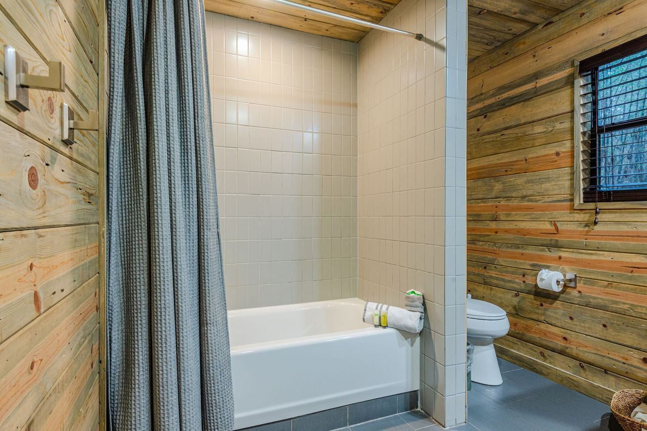 A bathroom with a wooden interior, a bathtub, a toilet, and a window.