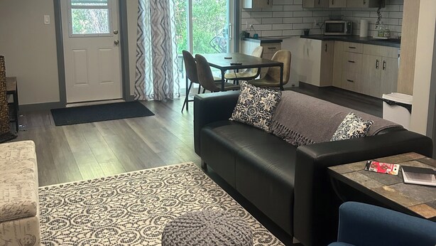 A modern living room with a sofa, ottoman, and blue armchair. There is a dining area with chairs and a table, and a kitchen with cabinets and appliances. - Ski, golf, hike or bike right outside your door if you like! (Kimberley)