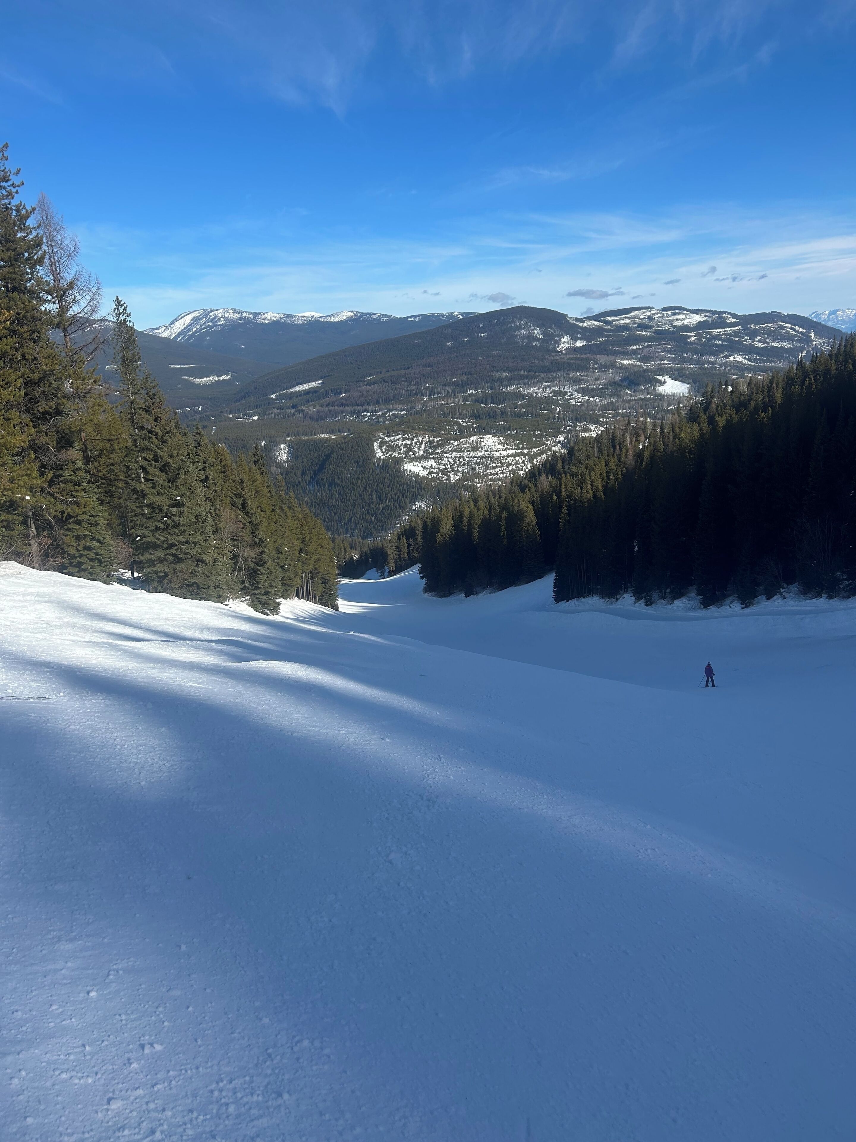 Un paysage de montagne enneigé, avec un skieur visible au loin.
