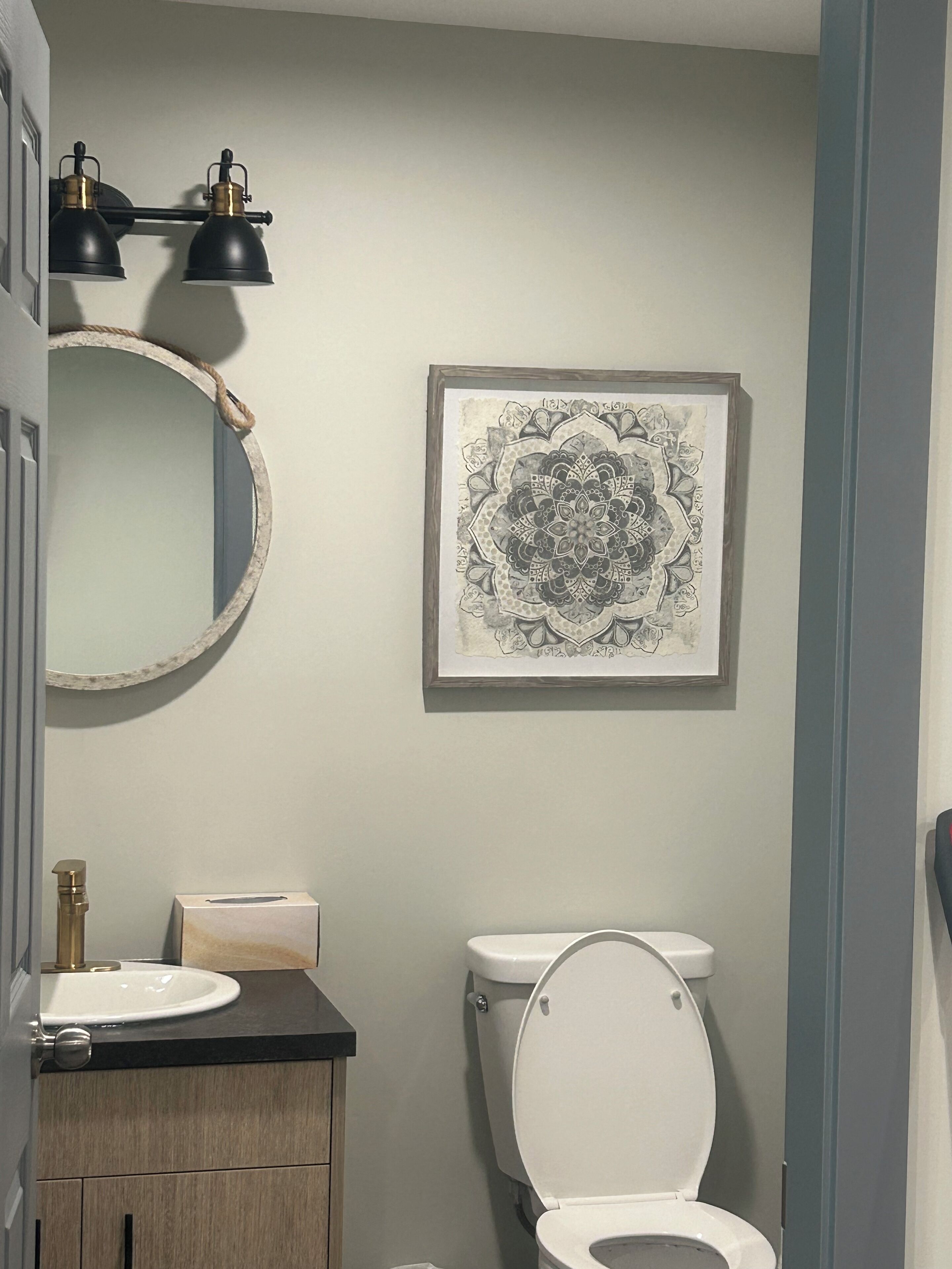 Een badkamer met een ronde spiegel, een wastafel, een toilet en een wanddecoratie met een mandala.
