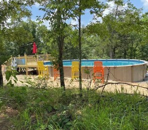 Une piscine dotée d’une terrasse en bois, entourée d’arbres et de verdure.