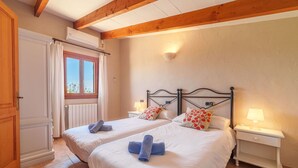 A bedroom with two beds, wooden beams, a window with curtains, a radiator, and bedside lamps. - Can Butxet by Interhome (Can Picafort)