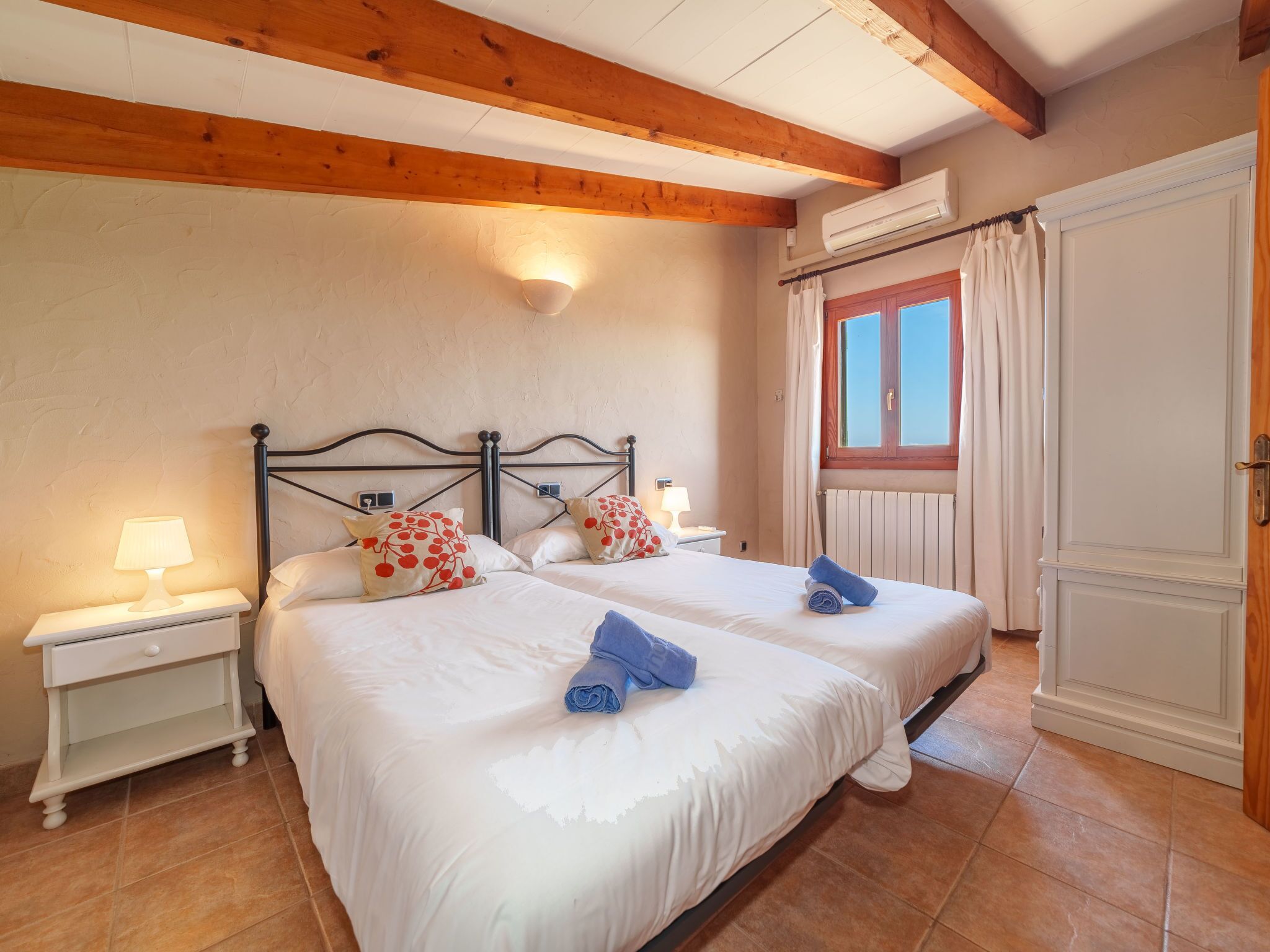 A double bed with white bedding and red polka dot pillows, a bedside table with a lamp, and a window with curtains.