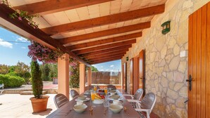 An outdoor dining area with a stone wall, wooden beams, and a view of the garden. - Can Butxet by Interhome (Can Picafort)
