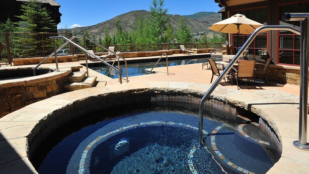 Ein Whirlpool mit Steinrand, einer Metallleiter und Blick auf Berge im Hintergrund.