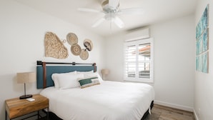 A bedroom with a bed, a nightstand, a ceiling fan, a window with blinds, and wall art.