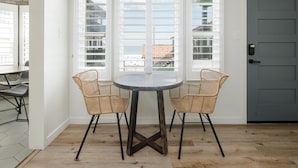 A dining area with a round table and two wicker chairs, a gray door, and a view of a balcony with a railing.