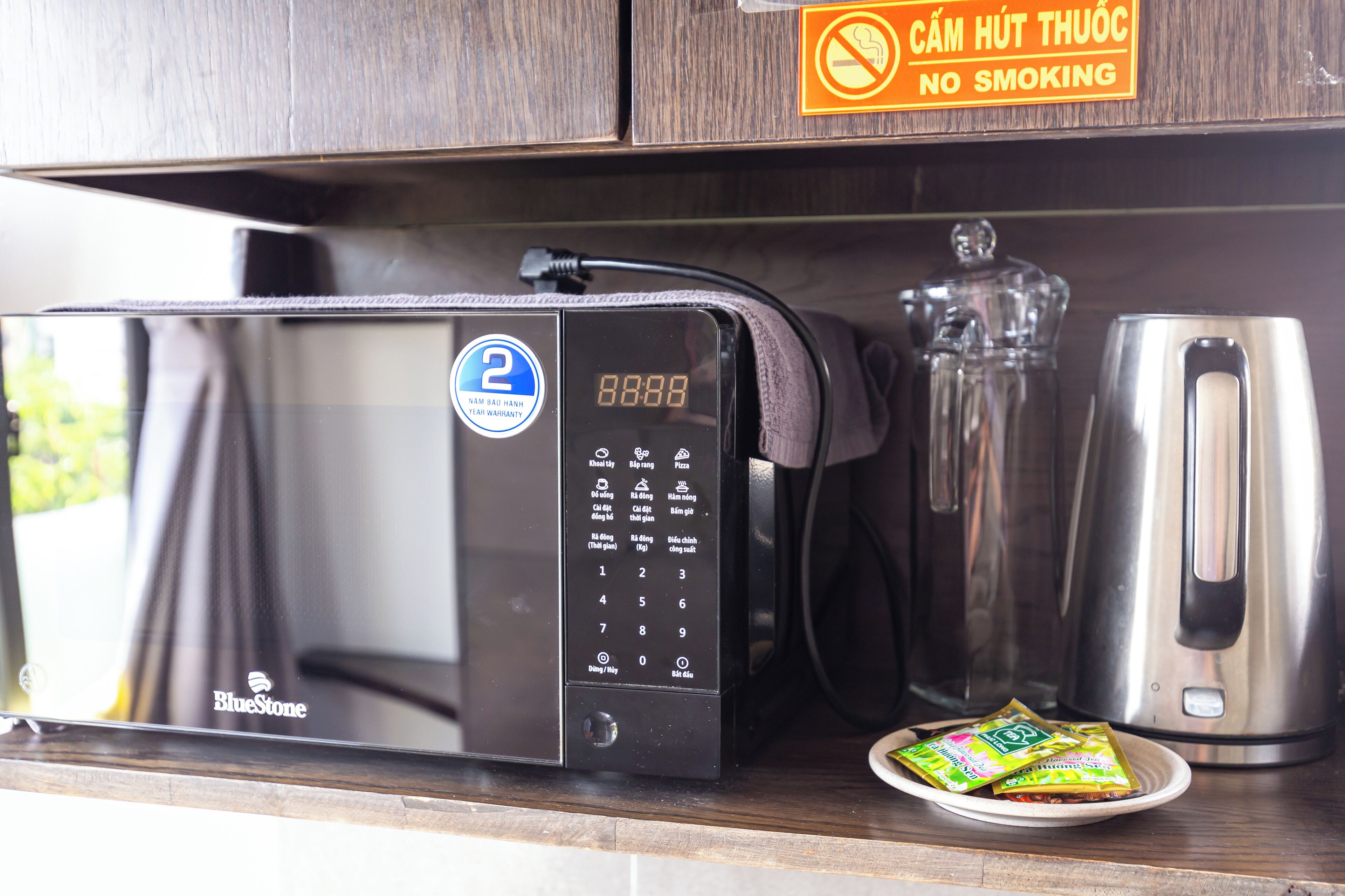 Un four à micro-ondes doté d’un écran numérique, une machine à café et une assiette avec des sachets, le tout posé sur un comptoir en bois.