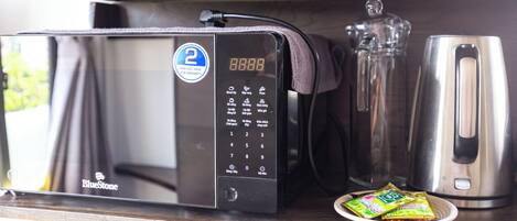 A microwave with a digital display, a coffee maker, and a plate with packets on a wooden countertop.