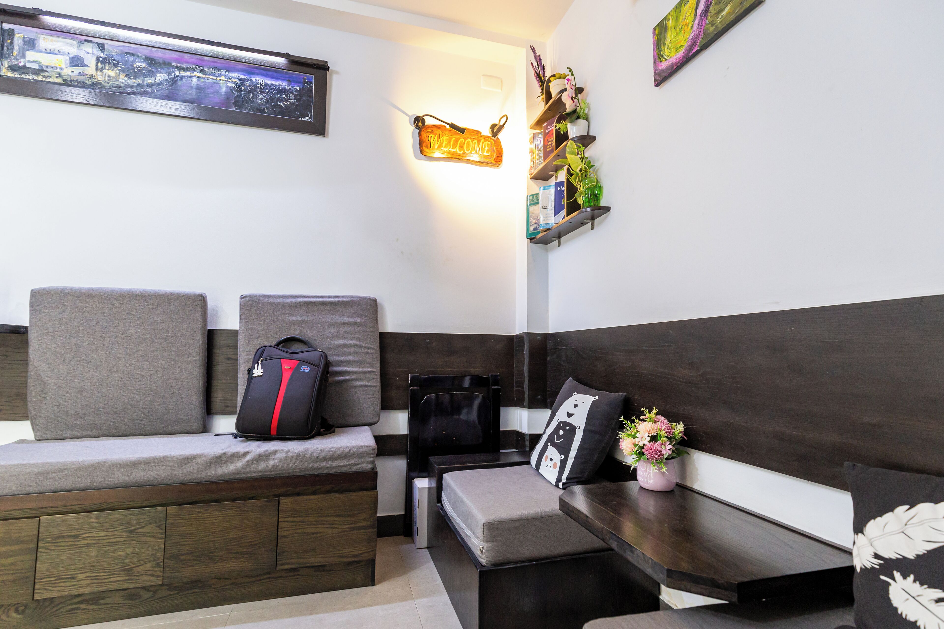 A modern hotel room with a sofa, a small table, a bench, and a wall-mounted shelf with decorative items.