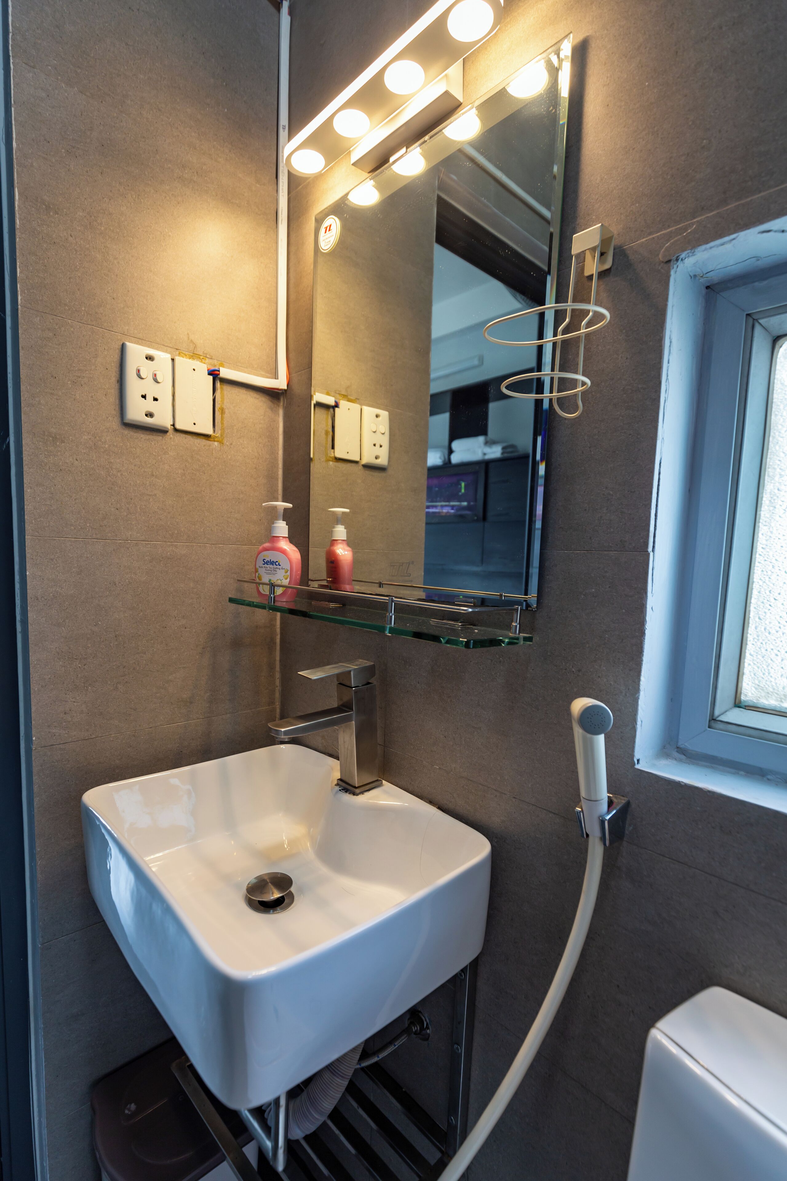 A bathroom with a white sink, mirror, and vanity. There are lights above the mirror and a showerhead to the right.