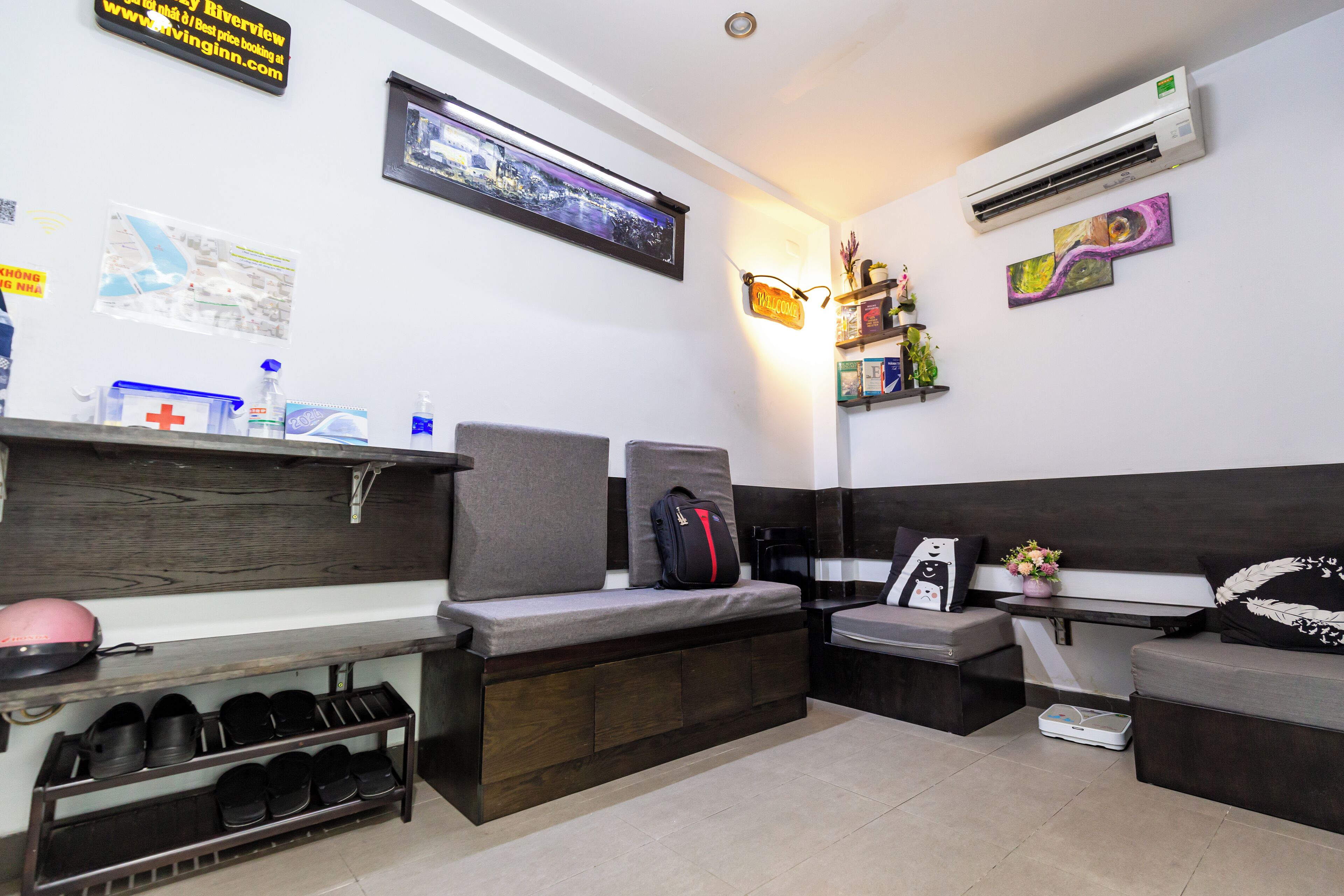 Habitación de hotel con cama, un banco, una mesita, estante con artículos de aseo y aire acondicionado de pared.
