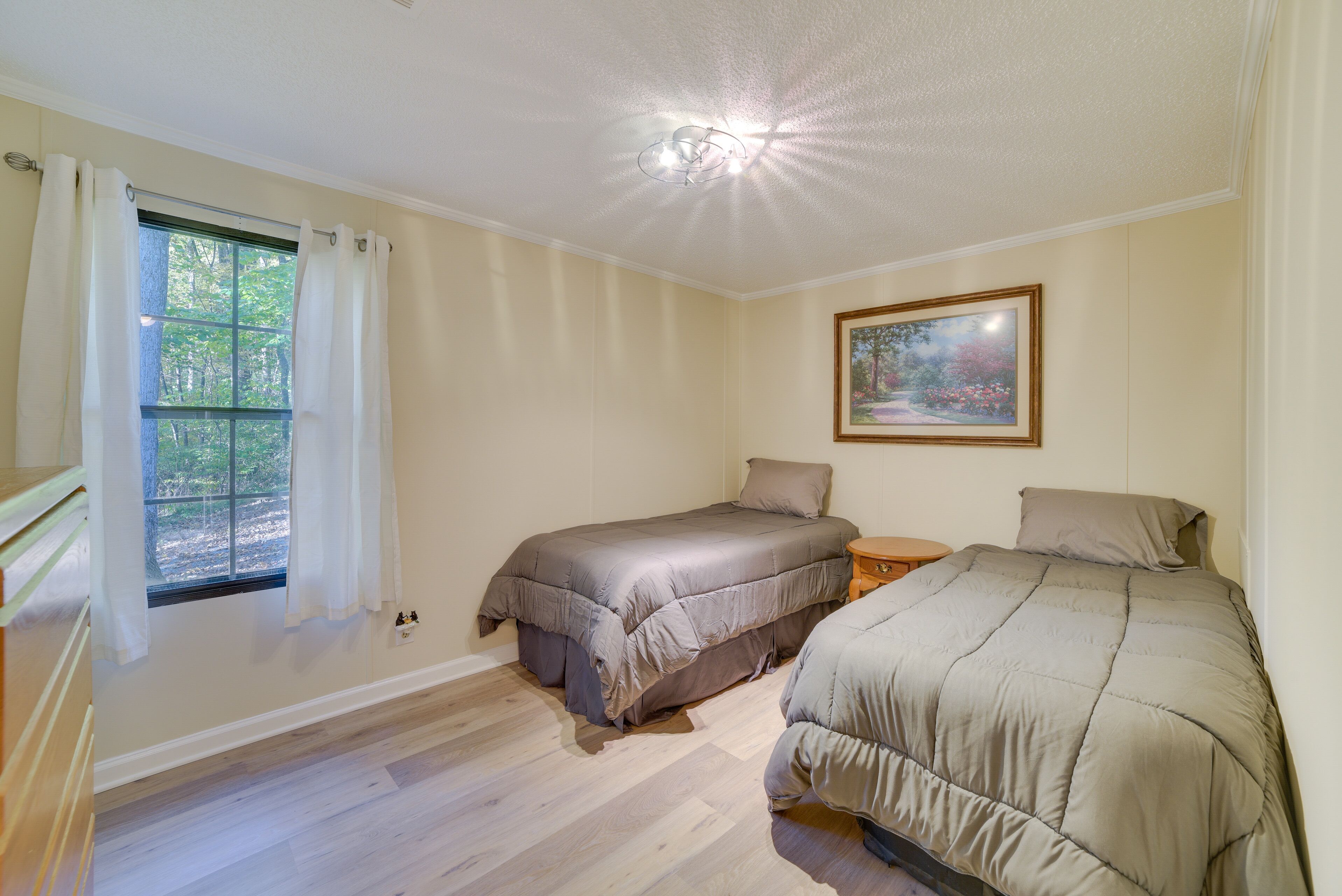 Un dormitorio con dos camas, una ventana con cortinas, un cuadro en la pared y una lámpara en el techo.