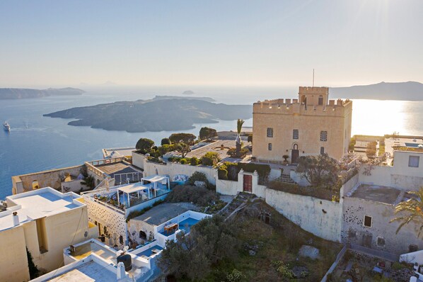 A coastal town with a prominent castle-like building, terraced rooftops, and a view of the sea and distant islands.