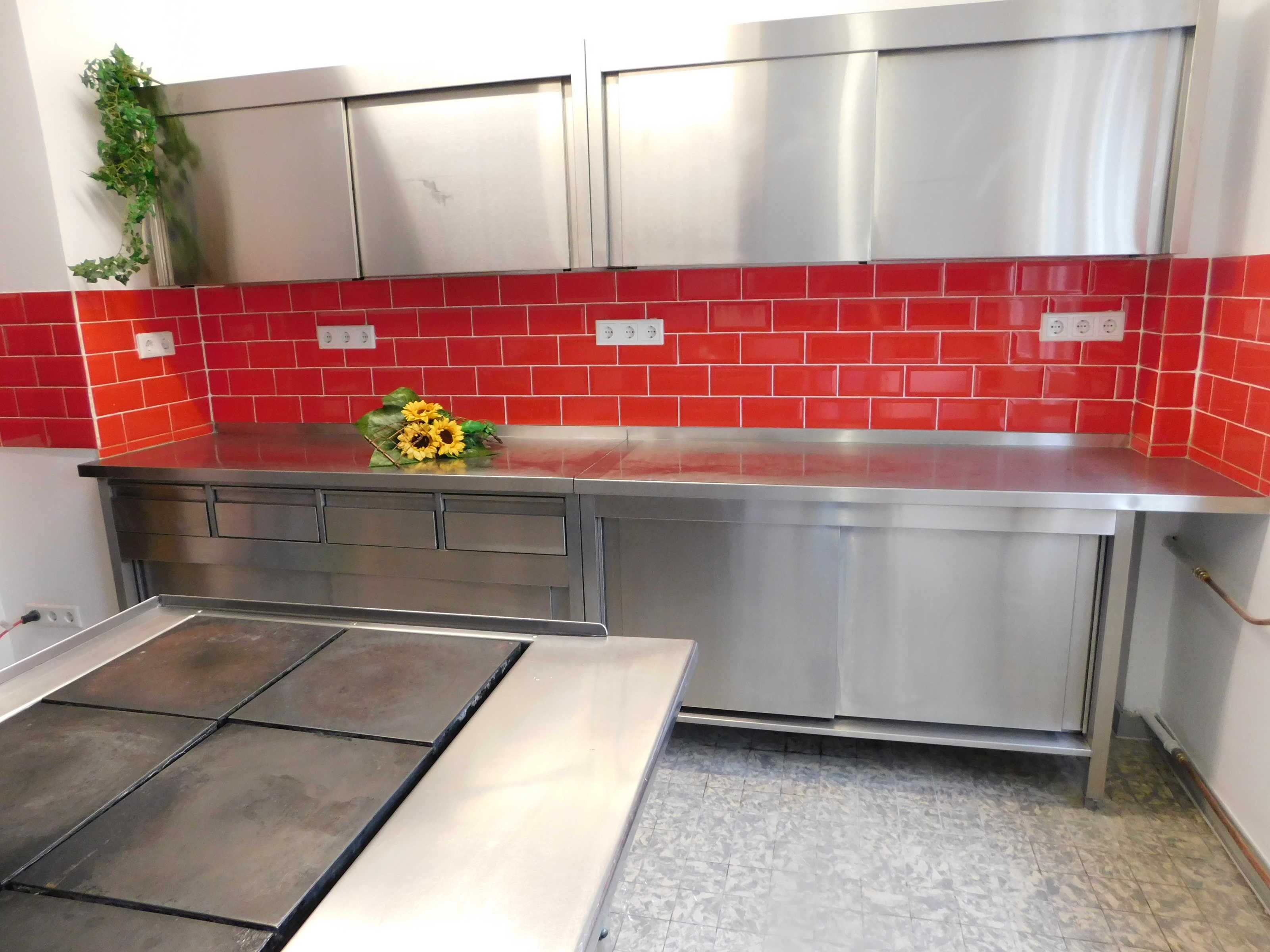 Een keuken met roestvrijstalen kasten, een rode tegelachtergrond en een aanrecht met een zonnebloemdecoratie.