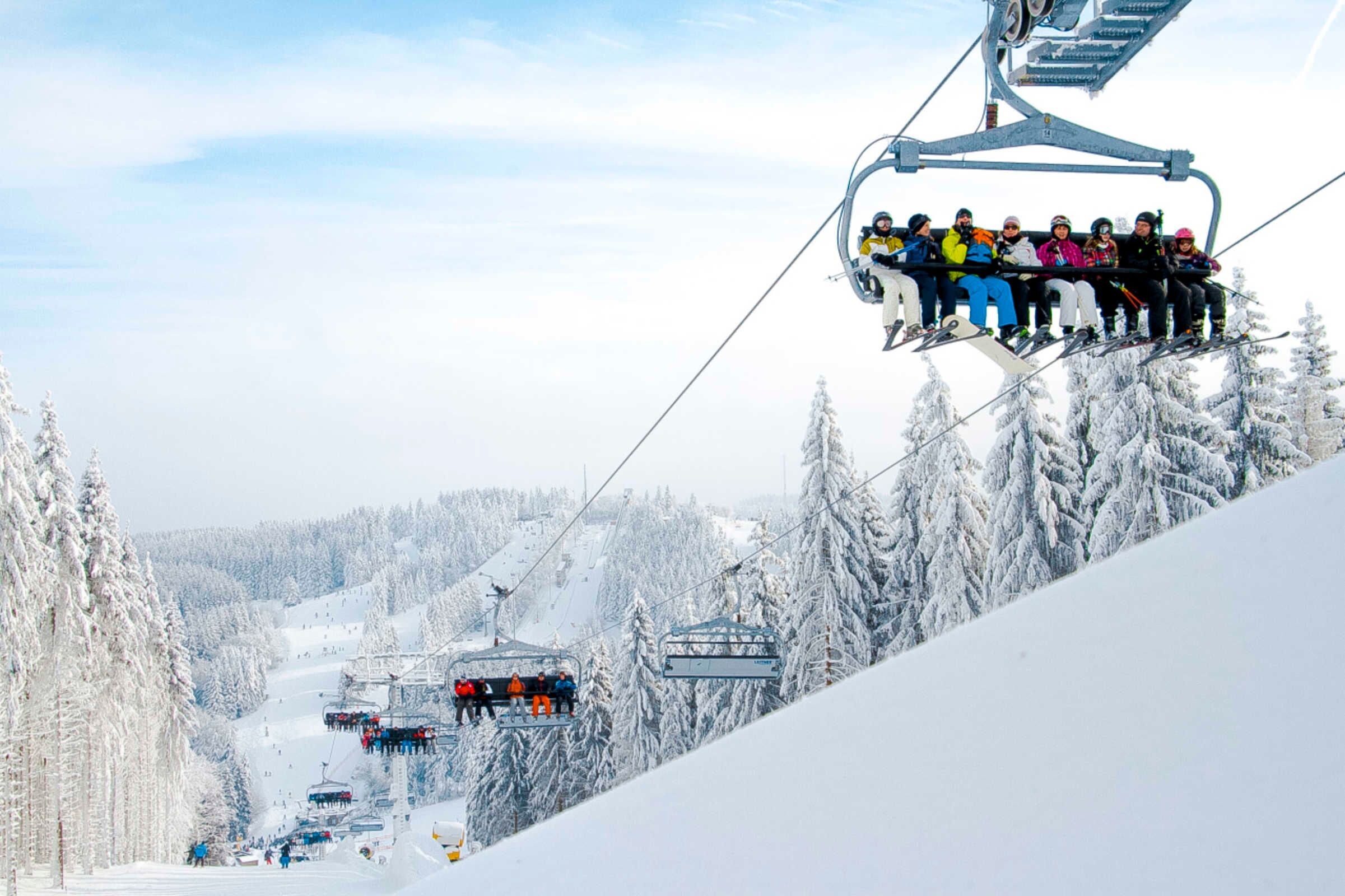 Un télésiège transportant des passagers, entouré d’arbres couverts de neige et d’un paysage hivernal.