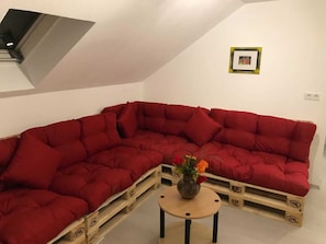 A red sectional sofa with a vase of flowers on a small round table. - Winterberg Apartment for 7 People - Astenblick Guesthouse, Also Suitable for Small Groups (Winterberg)