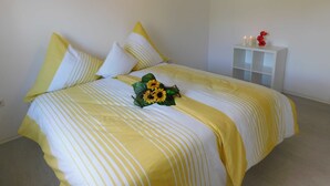 A bed with yellow and white striped bedding, a bouquet of sunflowers, and a white nightstand with candles. - Apartment Winterberg 7 persons - Guesthouse Astenblick also for small groups (Winterberg)