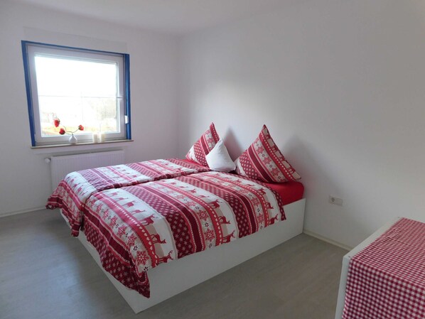 A bedroom with a bed, pillows, a window, and a radiator.