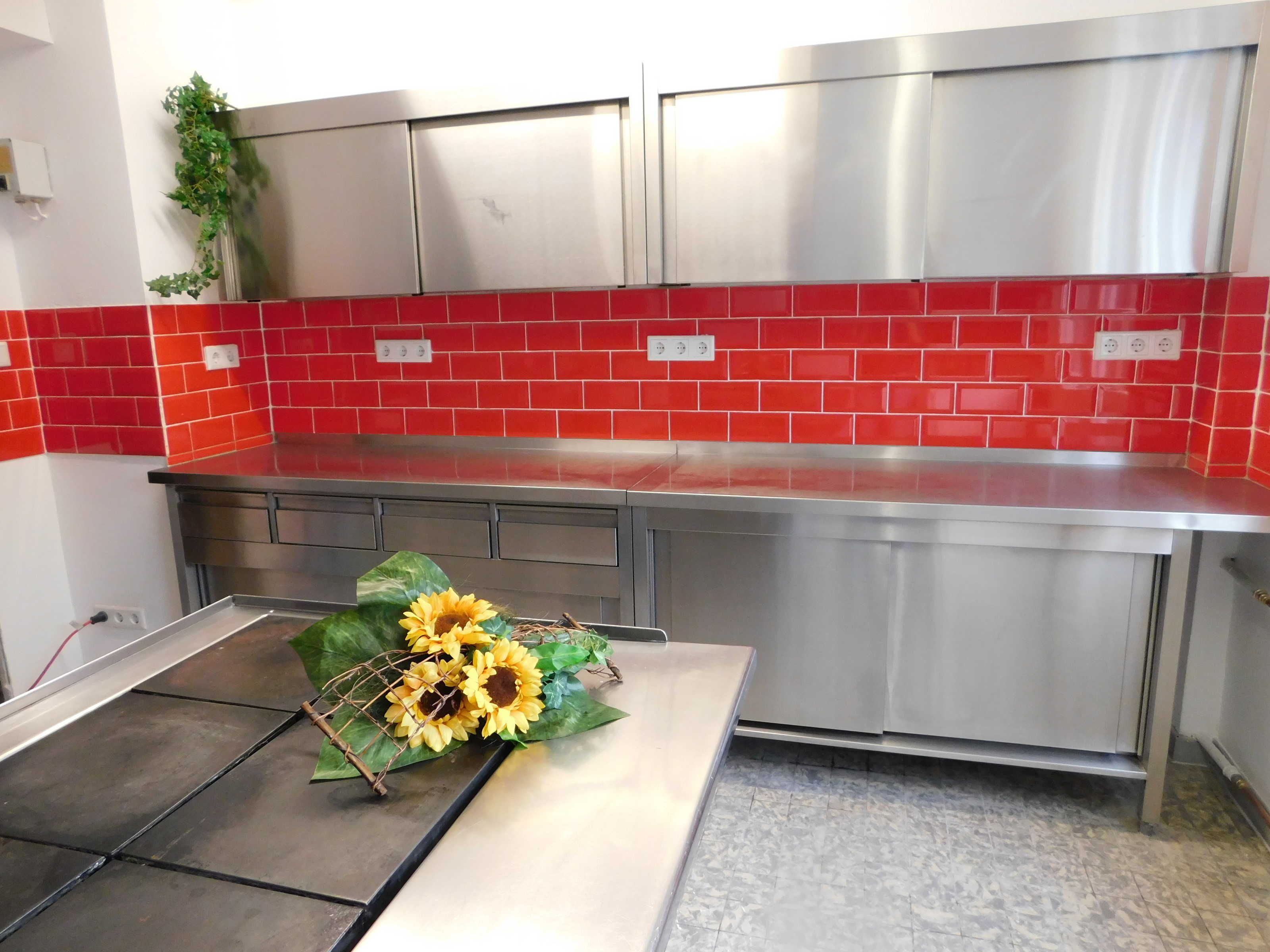 Een keuken met een rode betegelde spatwand, roestvrijstalen apparatuur en een decoratieve zonnebloemenboeket op het aanrecht.