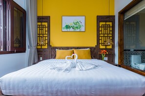 Una habitación de hotel con cama, paredes amarillas, un cuadro enmarcado y una ventana con cortinas.