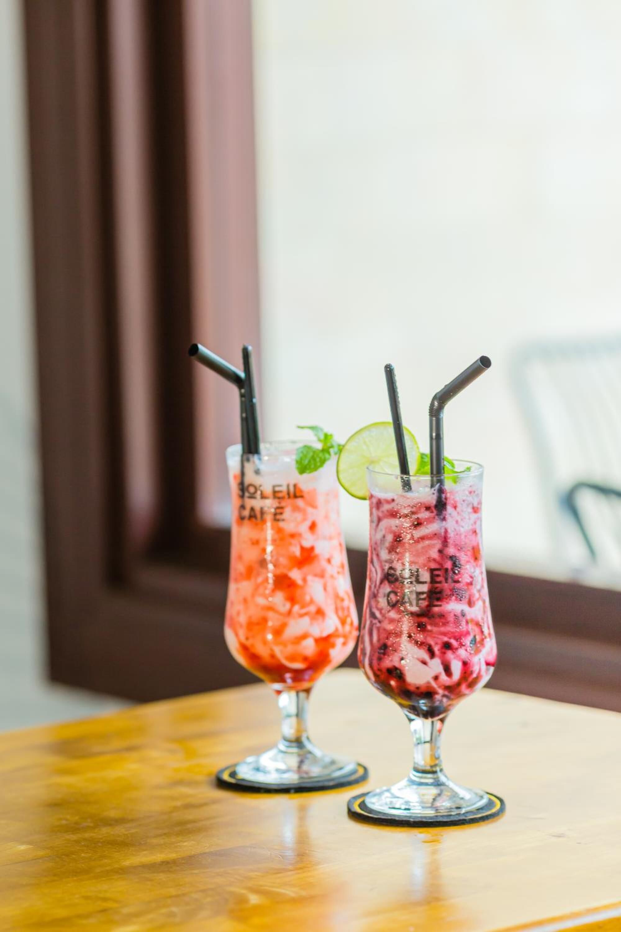 Two tall glasses of iced drinks with straws, garnished with mint and lime, on a wooden table.