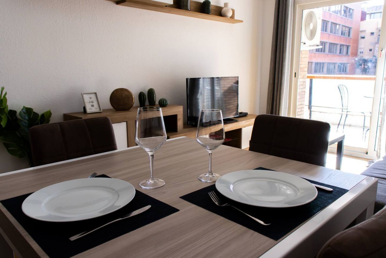 Une table à manger dressée avec des assiettes et des verres à vin, un téléviseur et une plante dans un salon moderne.