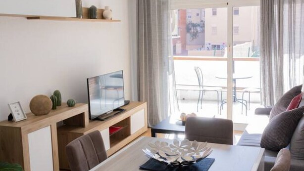 Ein modernes Wohnzimmer mit Fernseher, Sofa, Esstisch und Balkonblick.