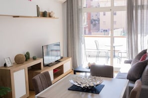 A modern living room with a TV, sofa, dining table, and a balcony view.