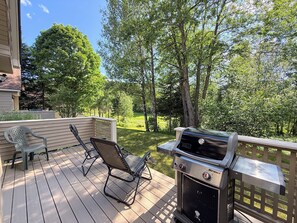 A deck with a grill, two chairs, and a view of a green landscape.